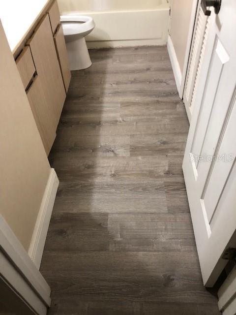 interior details featuring hardwood / wood-style flooring, shower / bathing tub combination, toilet, and vanity