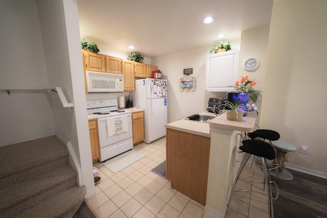 kitchen featuring a breakfast bar, light tile patterned floors, light brown cabinetry, and white appliances