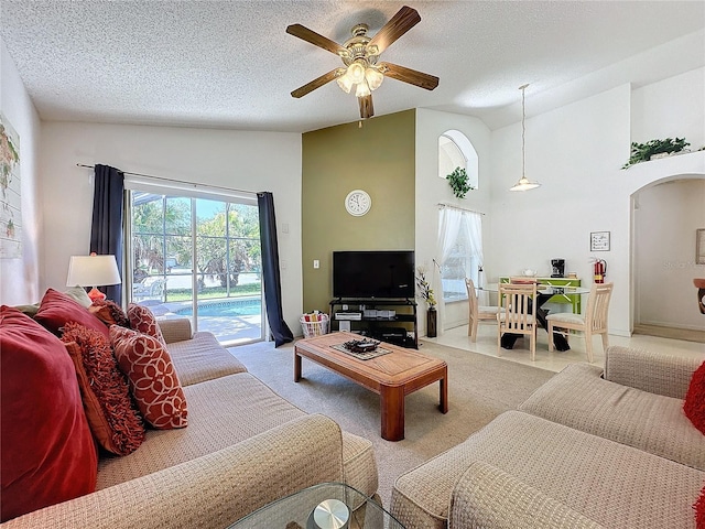 living room featuring a textured ceiling, high vaulted ceiling, light colored carpet, and ceiling fan