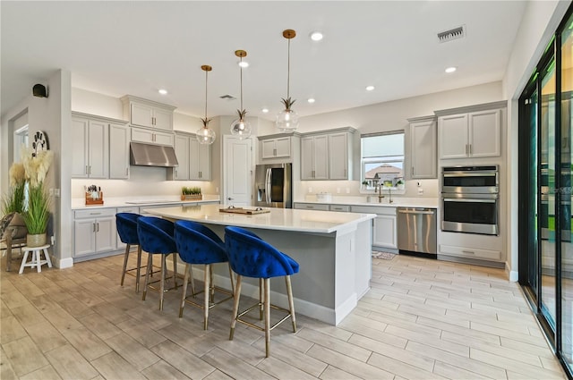 kitchen featuring gray cabinetry, hanging light fixtures, stainless steel appliances, a breakfast bar area, and a kitchen island