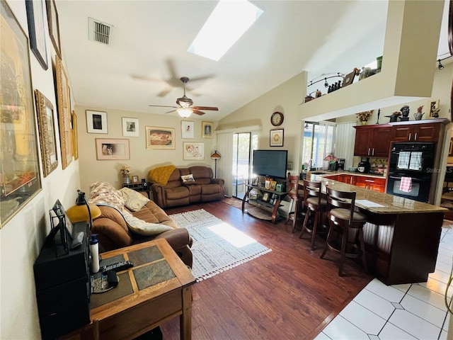 living room with ceiling fan, light hardwood / wood-style flooring, sink, and vaulted ceiling with skylight