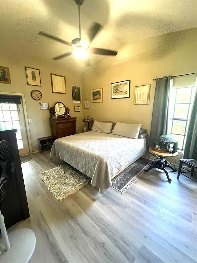 bedroom featuring ceiling fan, lofted ceiling, a textured ceiling, and light hardwood / wood-style flooring