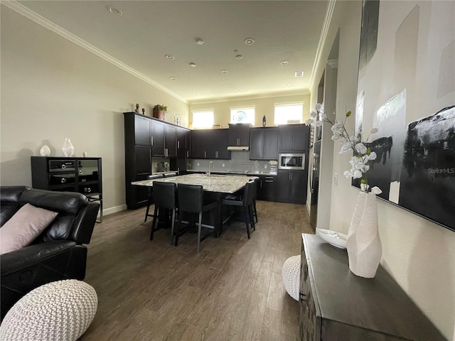 kitchen featuring a breakfast bar area, tasteful backsplash, stainless steel microwave, dark hardwood / wood-style flooring, and an island with sink