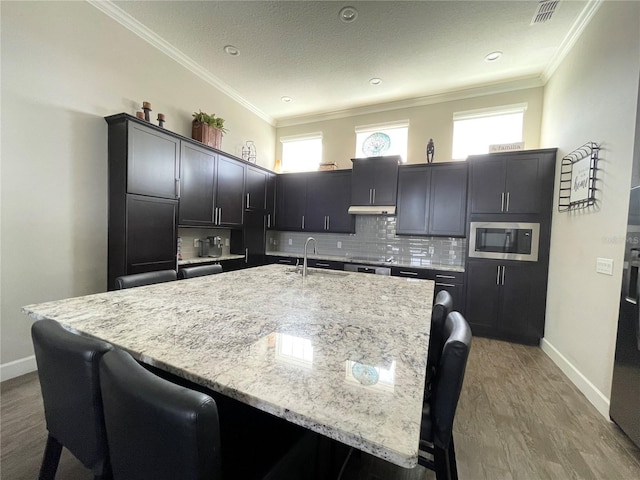 kitchen featuring built in microwave, sink, backsplash, and an island with sink