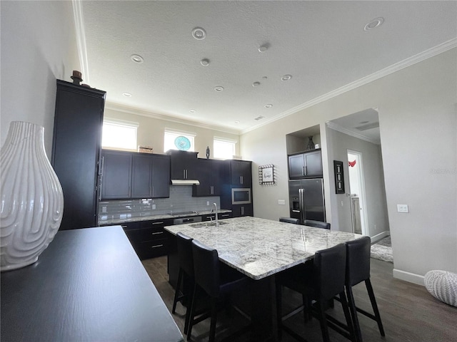 kitchen featuring a breakfast bar, appliances with stainless steel finishes, ornamental molding, an island with sink, and decorative backsplash