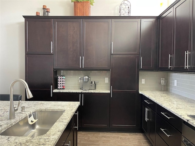 kitchen with sink, light hardwood / wood-style flooring, dark brown cabinets, light stone counters, and decorative backsplash