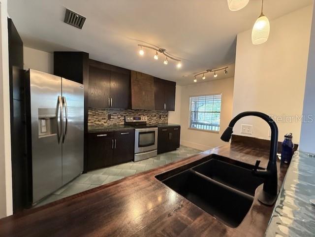 kitchen featuring sink, dark brown cabinets, stainless steel appliances, light tile patterned flooring, and decorative backsplash