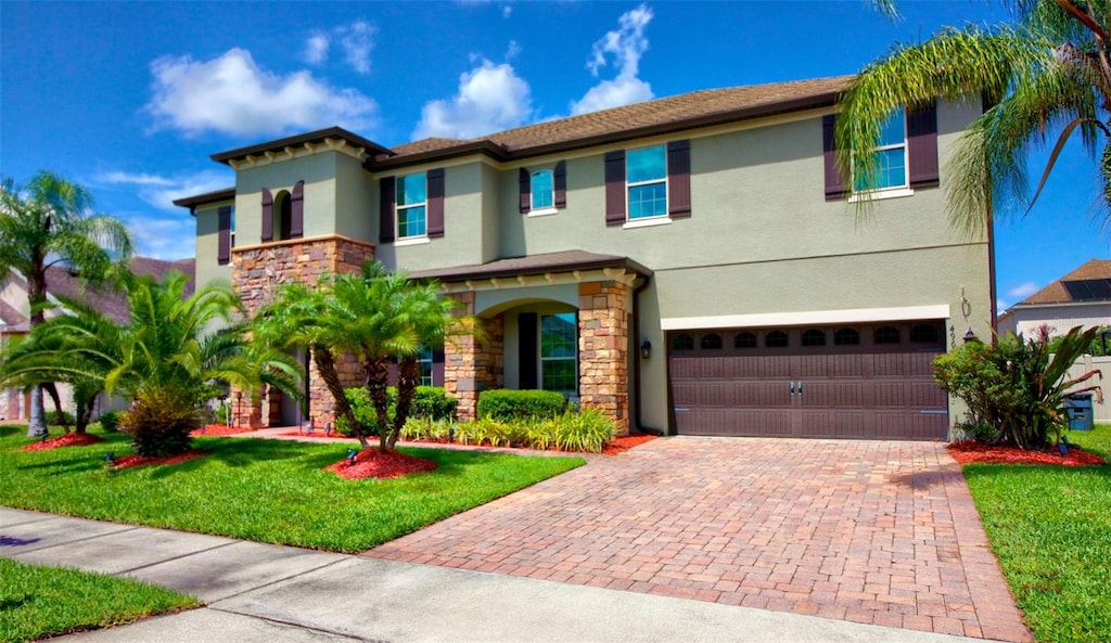 view of front facade with a front yard, an attached garage, stucco siding, stone siding, and decorative driveway