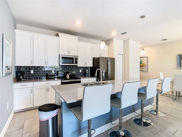 kitchen featuring light tile patterned flooring, white cabinetry, stainless steel appliances, hanging light fixtures, and backsplash