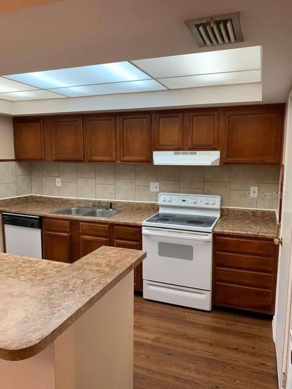 kitchen with dark wood-type flooring, sink, backsplash, and white appliances