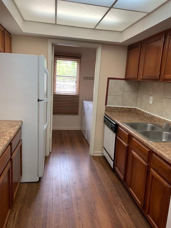 kitchen with sink, dark hardwood / wood-style floors, tasteful backsplash, and white appliances