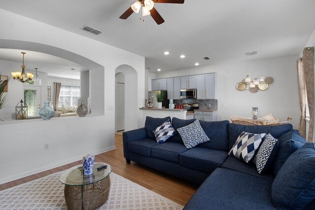 living room featuring ceiling fan with notable chandelier and light hardwood / wood-style flooring