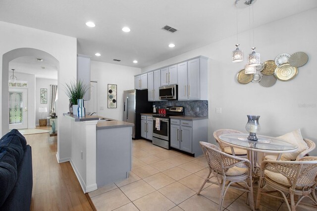 kitchen with pendant lighting, appliances with stainless steel finishes, gray cabinets, and backsplash