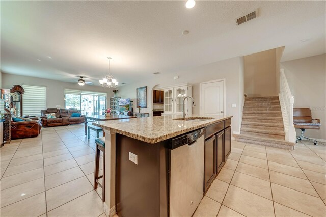 kitchen with light tile patterned floors, stainless steel dishwasher, hanging light fixtures, sink, and a center island with sink