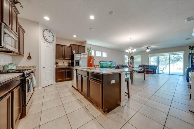 kitchen with light tile patterned flooring, sink, stainless steel appliances, and an island with sink