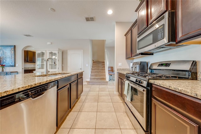 kitchen featuring light tile patterned floors, a textured ceiling, light stone countertops, appliances with stainless steel finishes, and sink