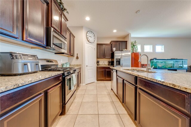 kitchen with light tile patterned flooring, sink, light stone counters, and stainless steel appliances