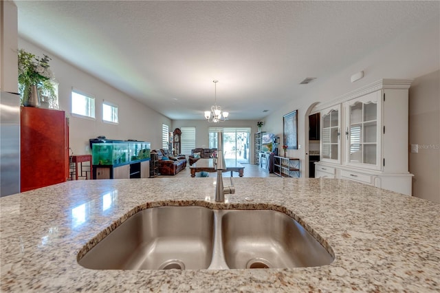 kitchen with a healthy amount of sunlight, light stone countertops, hanging light fixtures, and white cabinets