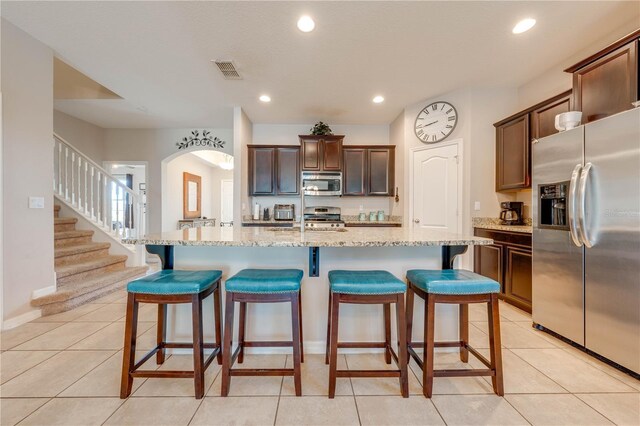 kitchen featuring a breakfast bar area, appliances with stainless steel finishes, light tile patterned floors, and an island with sink