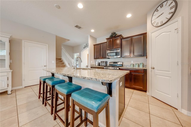 kitchen featuring sink, a kitchen bar, a kitchen island with sink, light tile patterned floors, and stainless steel appliances