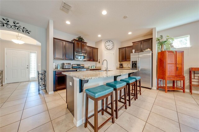 kitchen featuring sink, stainless steel appliances, light tile patterned floors, and an island with sink