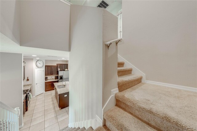 stairway featuring sink, light tile patterned floors, and a towering ceiling