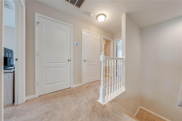 hall with light colored carpet and a textured ceiling