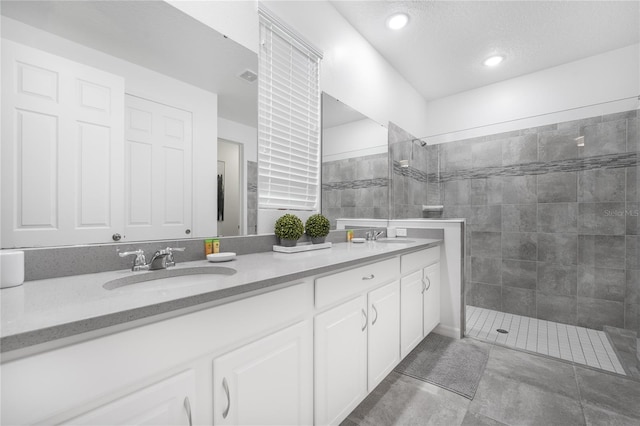 bathroom with tiled shower, double sink vanity, and tile patterned flooring