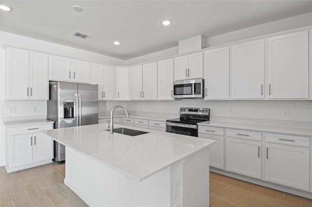 kitchen with sink, white cabinetry, a kitchen island with sink, appliances with stainless steel finishes, and light stone counters