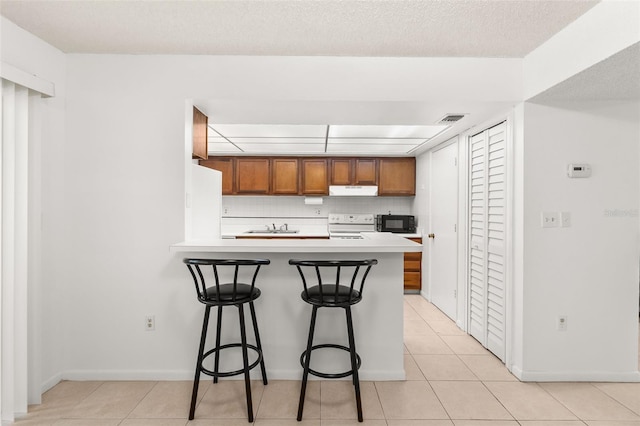 kitchen with light tile patterned flooring, a kitchen breakfast bar, brown cabinets, white appliances, and visible vents