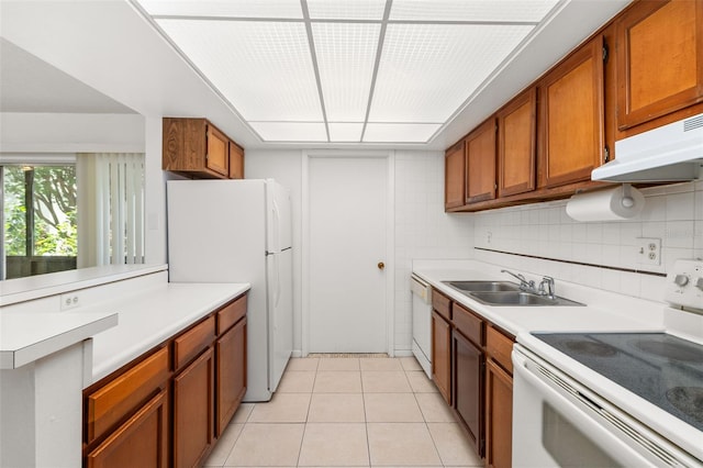 kitchen featuring light countertops, white appliances, under cabinet range hood, a sink, and brown cabinets