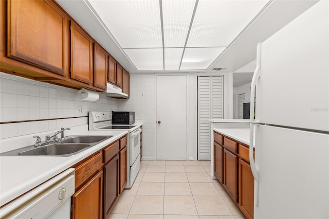 kitchen featuring white appliances, light tile patterned floors, under cabinet range hood, a sink, and brown cabinetry