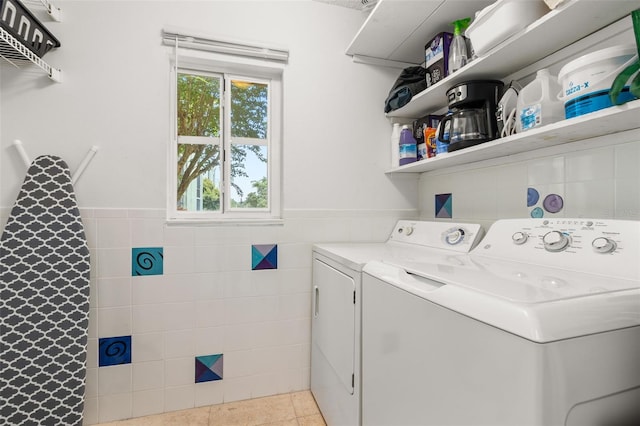 clothes washing area featuring light tile patterned flooring, tile walls, and washing machine and clothes dryer