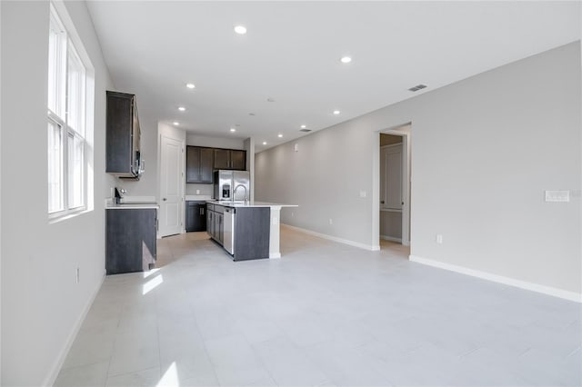 kitchen with dark brown cabinets, an island with sink, and stainless steel refrigerator with ice dispenser