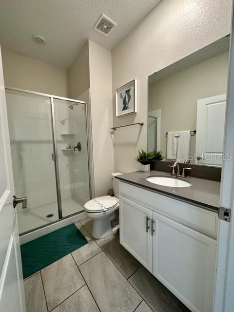 bathroom with tile patterned flooring, a shower with door, a textured ceiling, toilet, and vanity