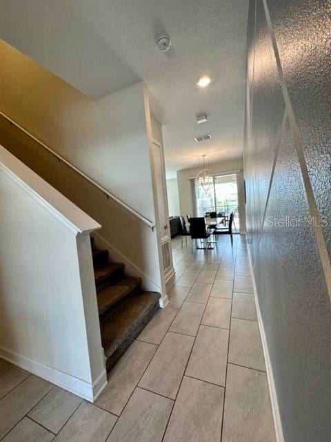 stairs with an inviting chandelier and light tile patterned floors