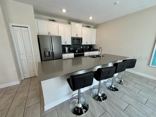 kitchen featuring a kitchen bar, stainless steel appliances, white cabinets, sink, and decorative backsplash