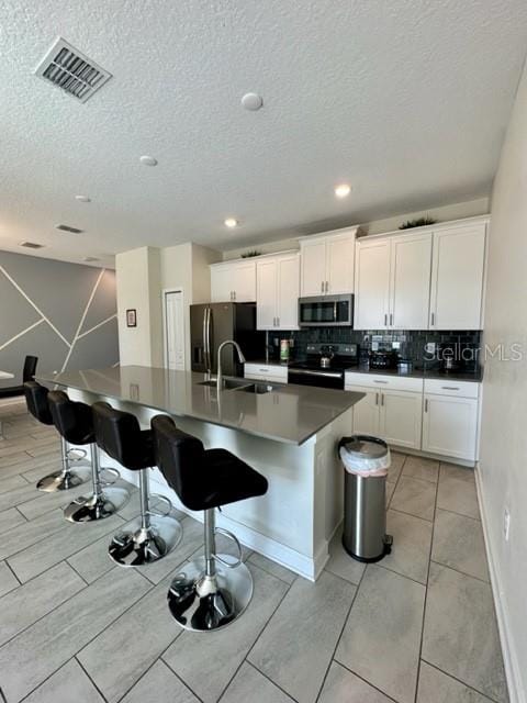 kitchen with white cabinets, stainless steel appliances, light tile patterned floors, decorative backsplash, and an island with sink