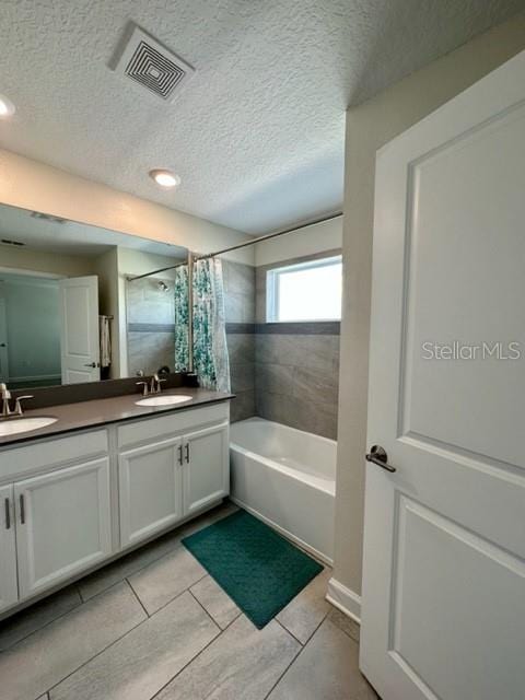 bathroom with dual vanity, a textured ceiling, tile patterned flooring, and shower / bath combination with curtain