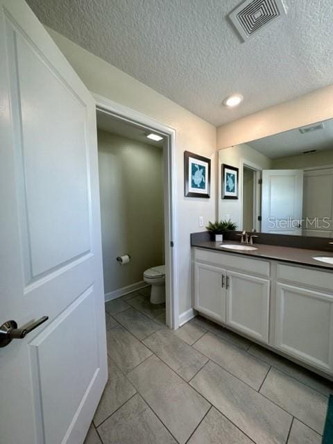 bathroom featuring vanity, tile patterned flooring, toilet, and a textured ceiling