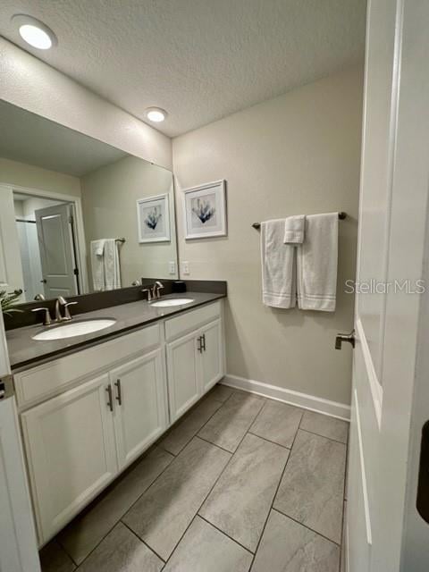 bathroom with tile patterned floors, a textured ceiling, and double vanity