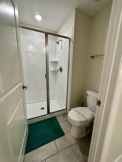 bathroom with a shower with door, a textured ceiling, toilet, and tile patterned floors