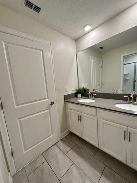 bathroom with a textured ceiling, tile patterned floors, and dual bowl vanity