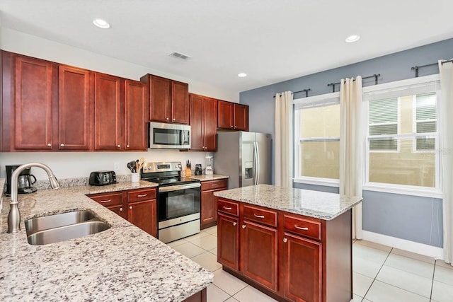 kitchen with appliances with stainless steel finishes, sink, light stone counters, and a kitchen island