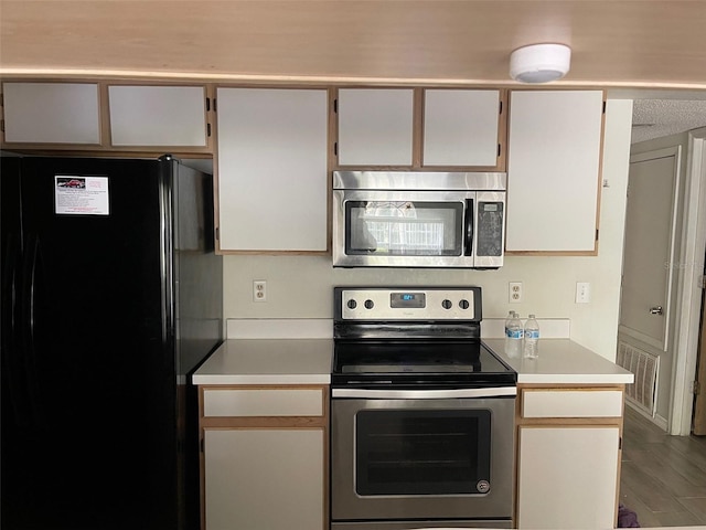 kitchen with appliances with stainless steel finishes, wood-type flooring, and white cabinets