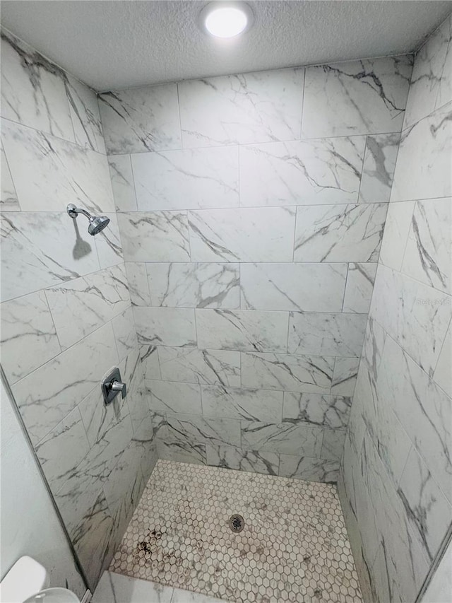 bathroom featuring toilet, a textured ceiling, and a tile shower