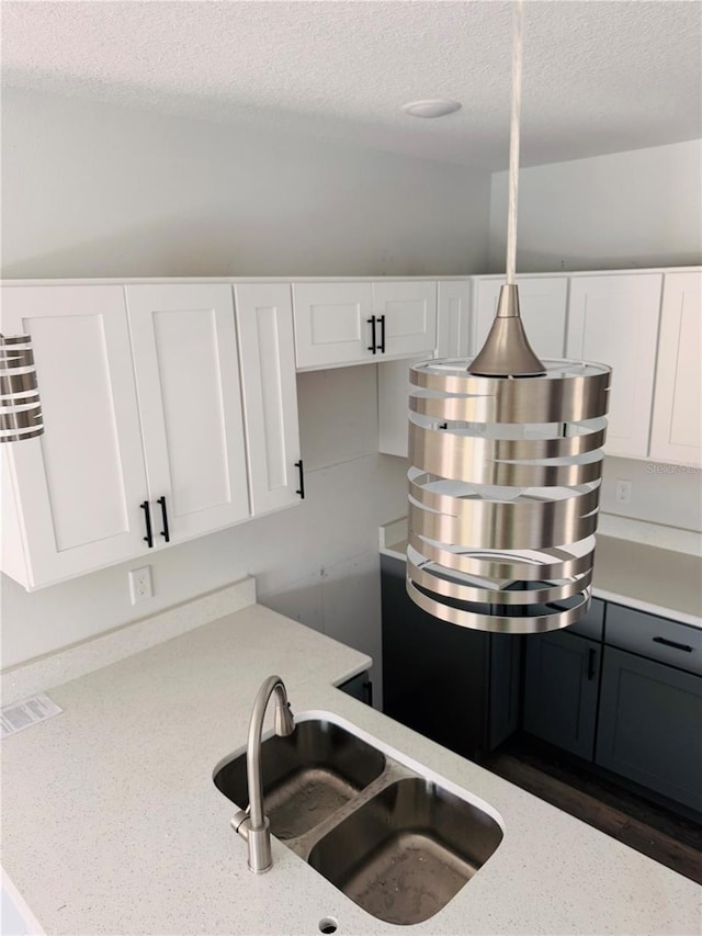 kitchen with light stone countertops, a textured ceiling, white cabinetry, and a sink