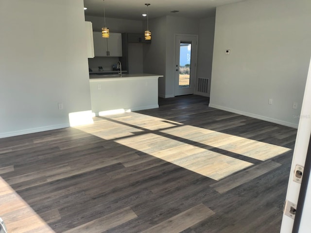 unfurnished living room with a sink, dark wood finished floors, visible vents, and baseboards