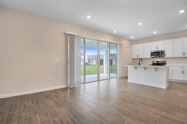 kitchen featuring sink, appliances with stainless steel finishes, a kitchen island with sink, white cabinets, and a kitchen bar