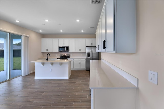 kitchen with a breakfast bar, sink, white cabinetry, a center island with sink, and appliances with stainless steel finishes